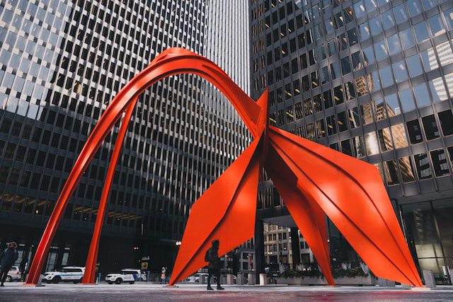 A 53-foot tall abstract sculpture of a red flamingo located near DePaul University in Chicago. The image is related to Chicago's public art and may be used to illustrate the city's unique and creative installations. It may also evoke feelings of wonder, curiosity, and appreciation for the arts.
