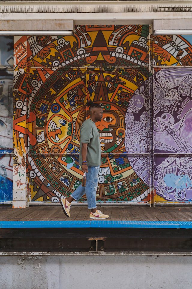 A man walking by street art in the Pilsen neighborhood of Chicago. The image is related to Chicago's urban culture and may be used to illustrate the city's street art, neighborhoods, or diversity. It may also evoke feelings of creativity, exploration, and community.