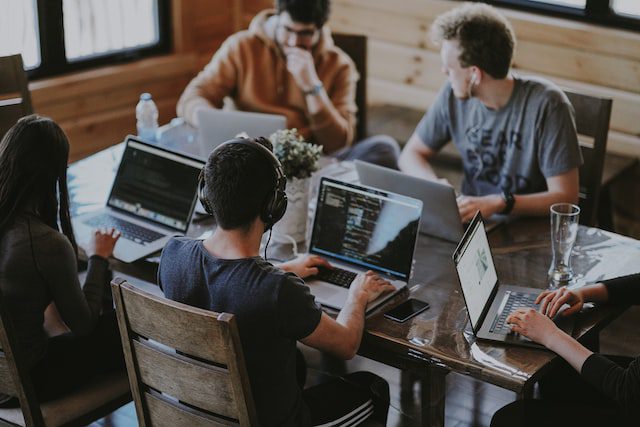 A diverse group of people sitting together and using a laptop computer - a great example of sharing a common space and working together. Get inspired by our 10 proven tips to break the ice with your new roommates and create a comfortable and collaborative living environment.