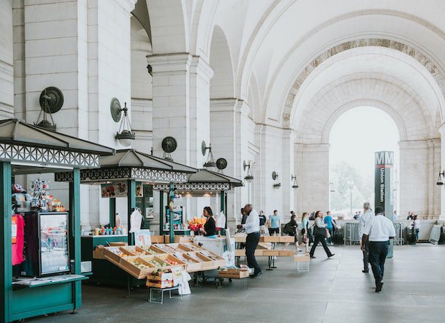 Union Station, a landmark white concrete building in Washington DC, with people walking under it. Learn about the 12 best neighborhoods in the city.