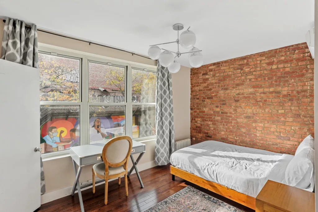 An eco-friendly furnished room with ample natural light streaming in through a large window and a convenient workspace for sustainable apartment living.