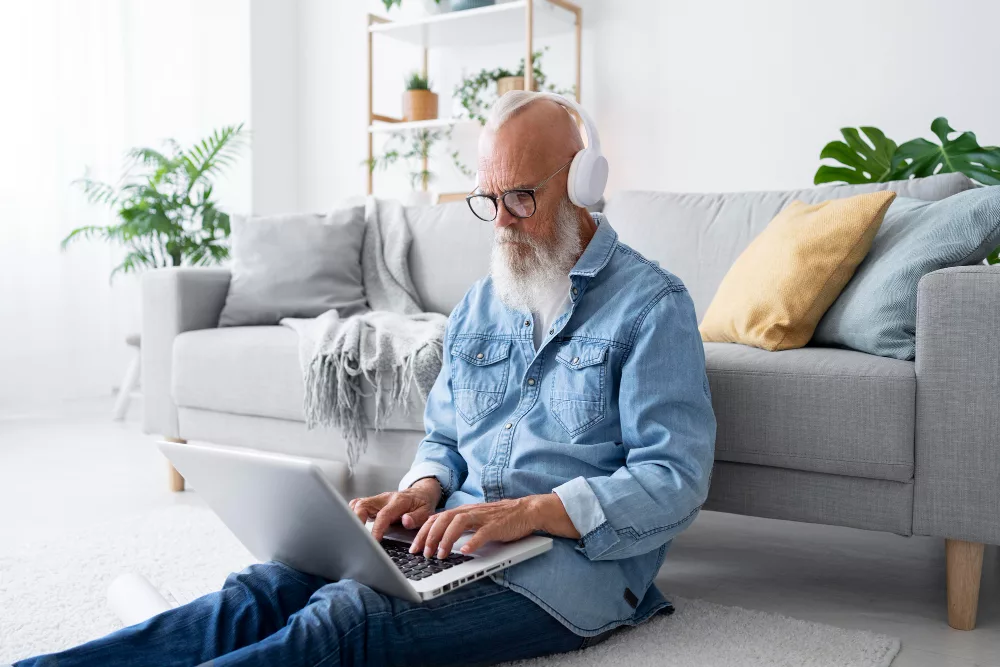 A man sitting on the floor with headphones, likely listening to music or a podcast in a common area of a shared living space. 