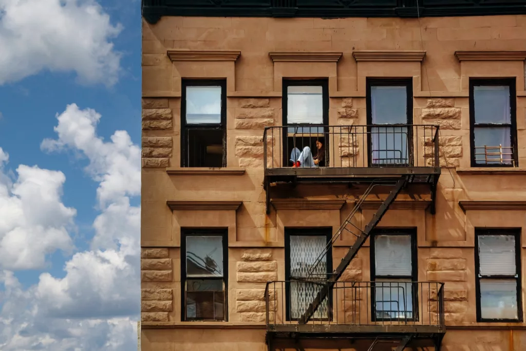 A woman relaxing on her sunny fire escape in a West Village walk-up building, perfect for Your Ultimate Guide to Moving to Manhattan