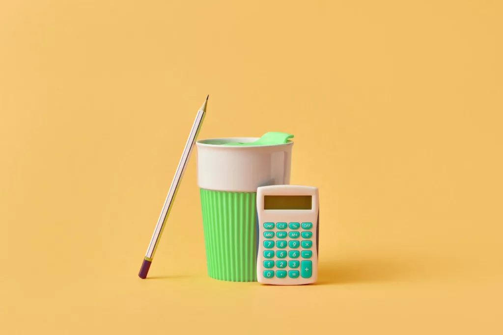 Pencil, calculator, and a cup labeled on a yellow background desk - Rent to Income Ratio Calculator Article.