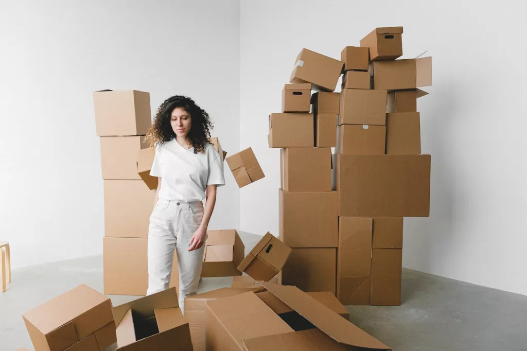A woman surrounded by heaps of cardboard boxes in her new house - a relatable scene for many millennials who prioritize mobility and flexibility. Learn why renting is the perfect solution for this demographic, allowing them to easily move to new cities or neighborhoods and explore different opportunities while enjoying the comforts of a new home.