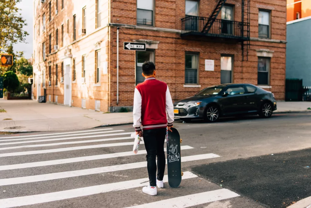 Man in red and white long sleeve shirt and black pants walking on pedestrian lane in Queens, NYC