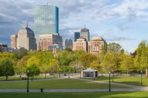 Green grass field with trees and buildings in distance under white clouds and blue sky during photo