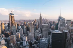 A panoramic view of New York City at dusk, showcasing the dense skyline with the iconic Empire State Building in the foreground and various skyscrapers stretching into the distance under a soft golden sky.