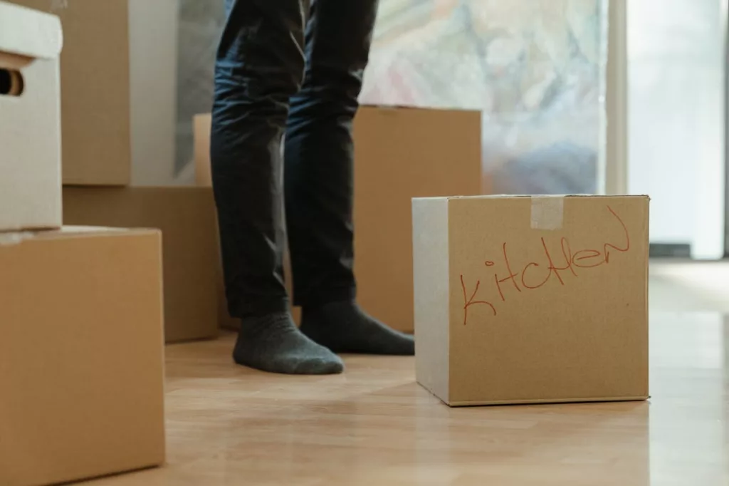 A person stands next to a labeled cardboard moving box.