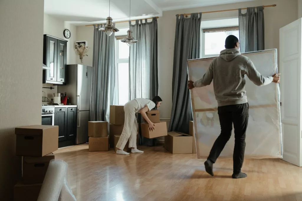 Woman holding cardboard boxes while a man holds a big painting