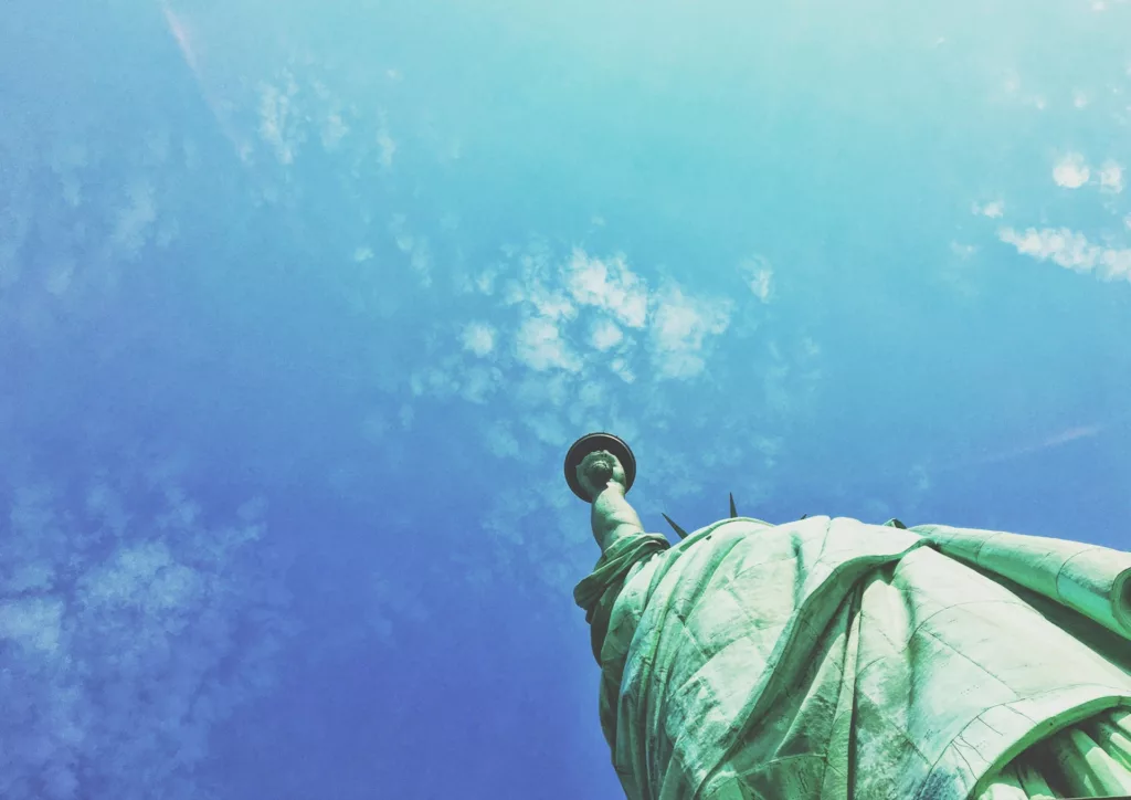 Statue of Liberty viewed from below against a bright blue sky with scattered clouds, symbolizing hope and new beginnings, relevant to an article about the best housing options for US immigrants.