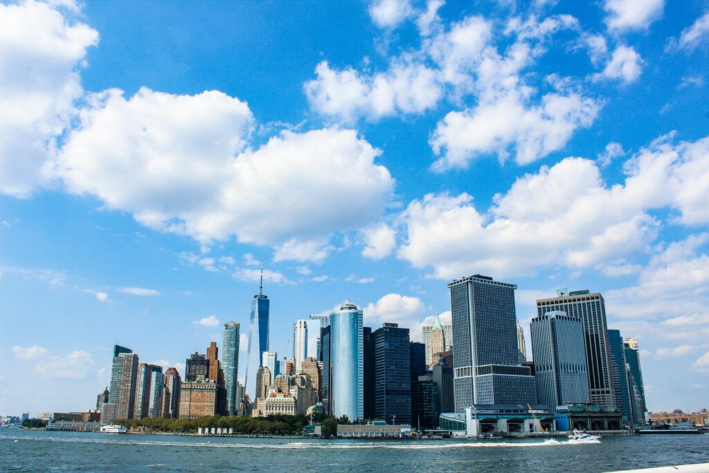 View of Lower Manhattan skyline from the water under a bright blue sky with scattered clouds, representing an attractive location for intern housing in New York City, offering proximity to key business districts and vibrant urban life.