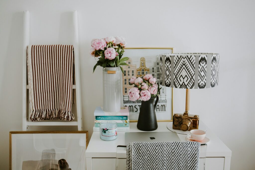 Cozy rental apartment decor setup featuring a striped throw blanket on a ladder, a vase of pink flowers, framed artwork, and a patterned lampshade, showcasing easy ways to personalize a rental without altering the property.