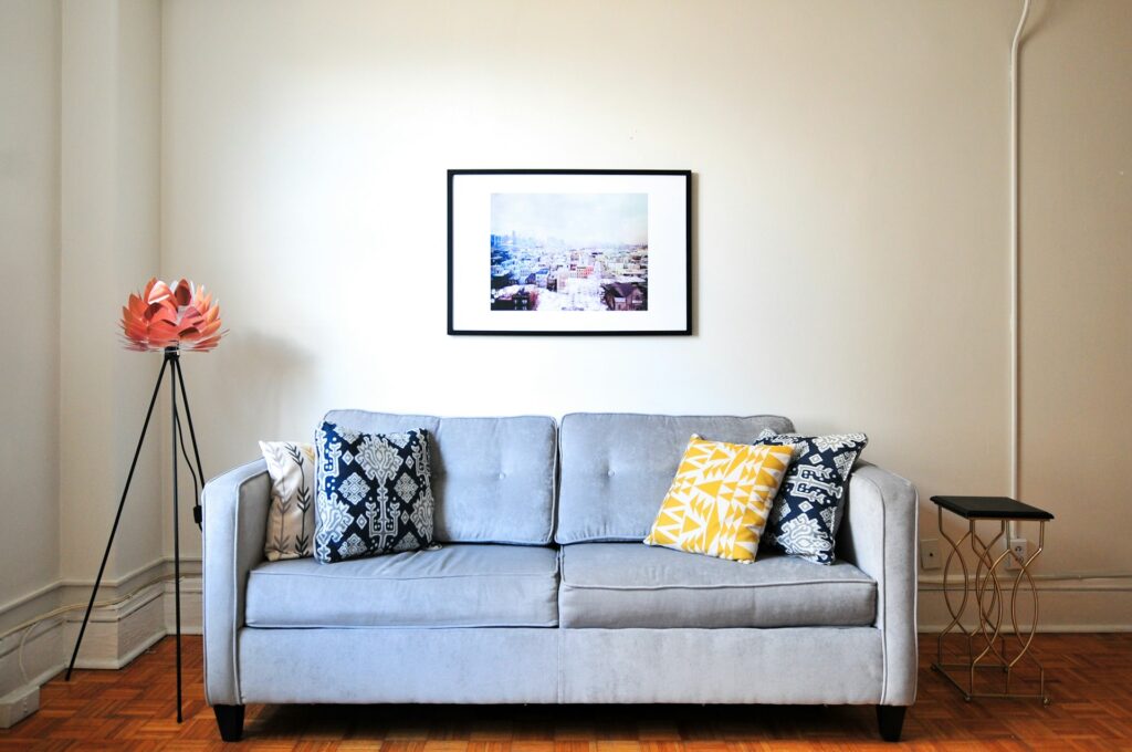 A cozy living room with a gray sofa adorned with decorative pillows, a modern floor lamp, a framed artwork on the wall, and a small side table.