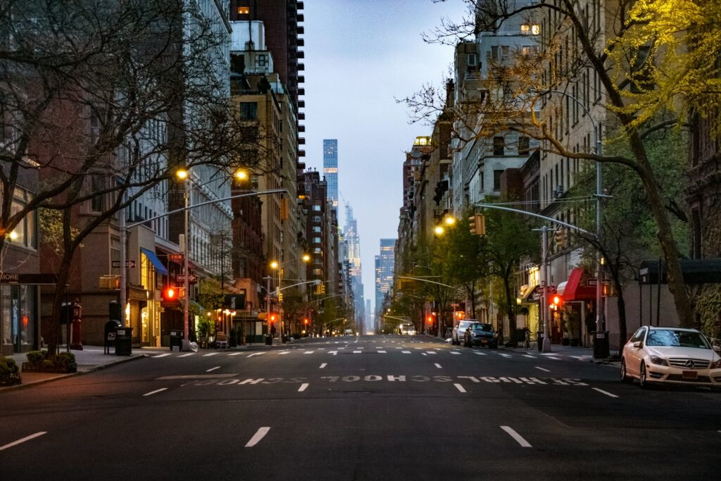 A serene evening view of a wide, tree-lined avenue in the Upper East Side of New York City, showcasing elegant buildings, streetlights, and a few cars, capturing the essence of urban living.